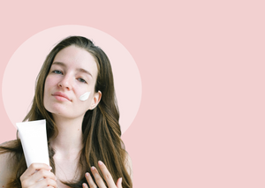 Woman applying cream to her face with a pink background